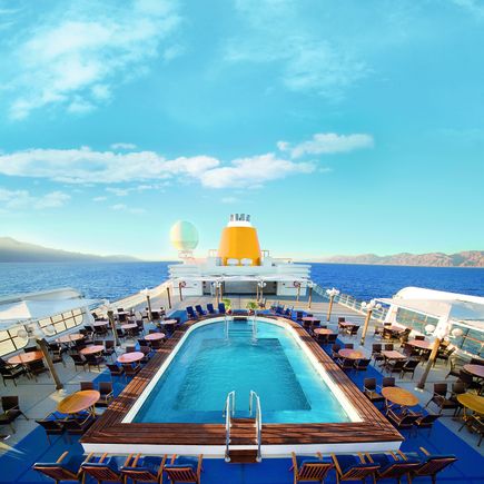 Blick auf das Deck der MS Hamburg mit Pool und Liegen und Tischen mit Stühlen am Poolrand. 