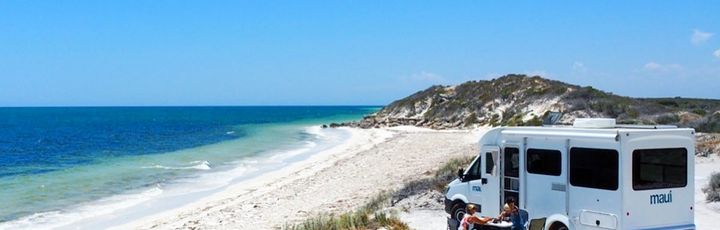 Camper steht an einer Straße am kristallklaren Strand in Australien