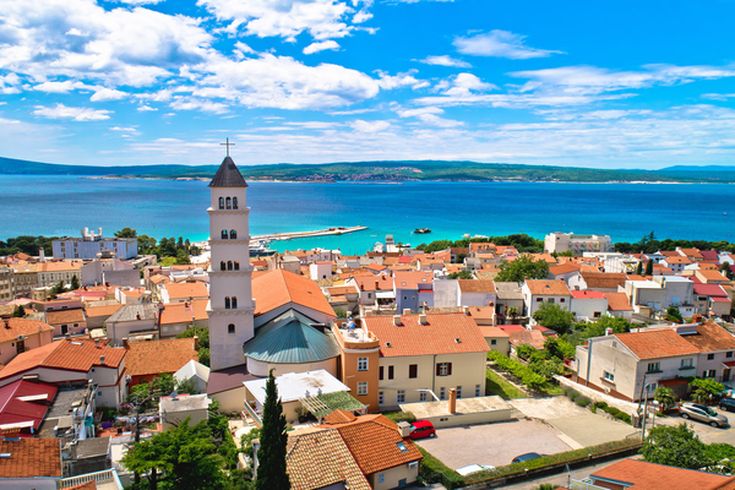 Eine Stadtansicht von Crikvenica mit roten Dächern und Blick auf das Meer und einen Kirchturm.