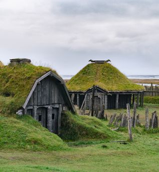 Zwei mit Moos bewachsene Holzhütten an einem Gewässer in Island