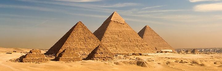 Weitläufiges Wüstenpanorama mit den eindrucksvollen Pyramiden von Gizeh vor der nahen Skyline Kairos.