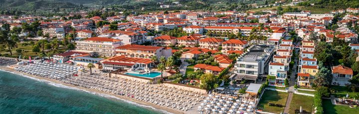 Blick auf Hanioti aus der Vogelperspektive. Breiter Strand mit Liegen, dahinter Grün und Häuser.