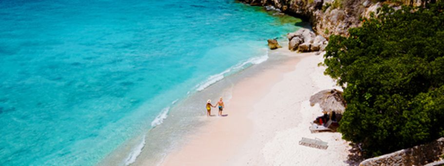 Ein Sandstrand mit türkisfarbenem Wasser, umgeben von Felsen und Bäumen.