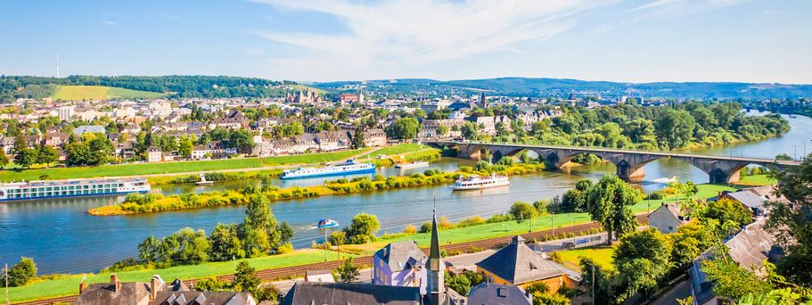 Eine Stadtansicht mit einem Fluss und Gebäuden, umgeben von grünen Hügeln.