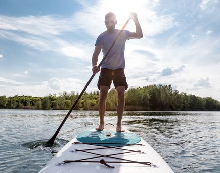 Eine Person steht auf einem Stand-Up-Paddle-Board auf einem ruhigen See und paddelt.