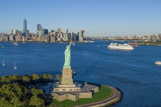 Blick über das Meer auf die Freiheitsstatue, im Hintergrund ein AIDA Schiff