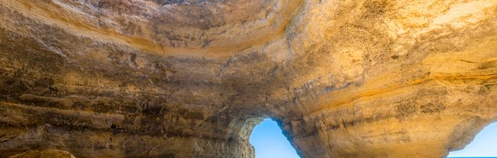 Eine natürliche Höhle mit einem Bogen, der zum Meer führt, beleuchtet von der Sonne.