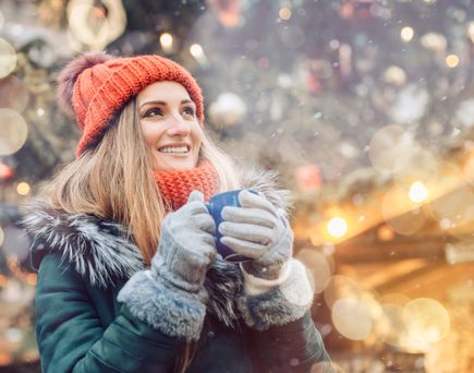 Frau auf Weihnachtsmarkt trinkt heißen Tee
