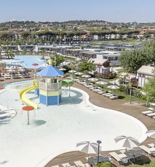 Großer Aquapark mit Wasserrutsche, Sonnenschirmen und Liegestühlen, umgeben von Mobilheimen und grüner Landschaft.