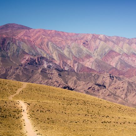 Die farbenprächtigen Hornocal-Berge in der Quebrada de Humahuaca, Argentinien, zeigen beeindruckende Schichten in Rosa-, Rot- und Gelbtönen unter einem blauen Himmel.