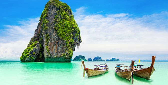 3 typisch thailändische Boote vor Felsen an einer Küste in Thailand