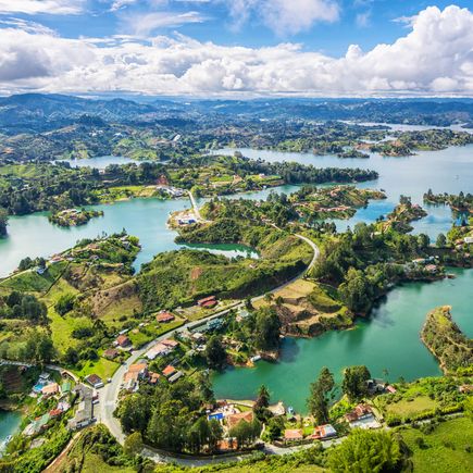 Der imposante Felsen El Peñón de Guatapé in Kolumbien, umgeben von einem großen Stausee und grünen Hügeln, mit einer Treppe, die zur Spitze führt.