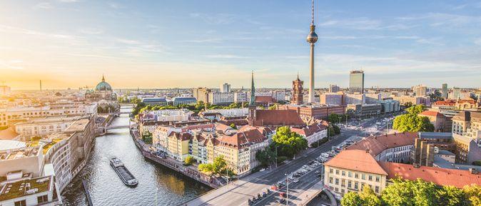 Panoramaaufnahme der Berliner Innenstadt mit dem Fernsehturm, Berliner Dom und Spreefluss bei klarem Himmel und Sonnenlicht.
