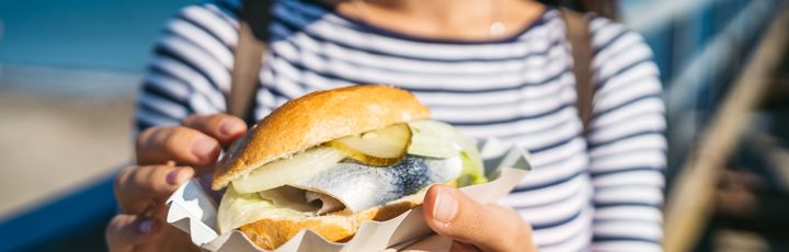 Eine Frau halt ein gut gefülltes Fischbrötchen in der Hand.