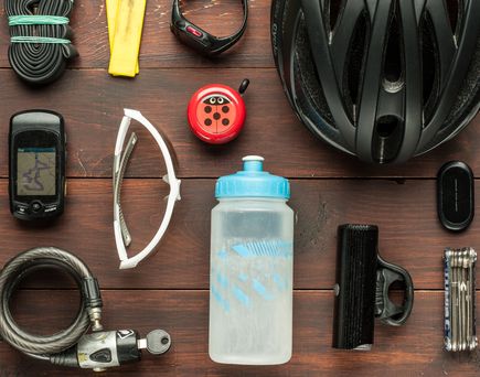 Verschiedenes Fahrrad-Equipment wie Helm, Handschuhe, Flasche und Werkzeug auf einem Holzuntergrund.