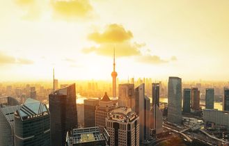 Die beeindruckende Skyline von Shanghai bei Sonnenaufgang, mit zahlreichen beleuchteten Wolkenkratzern und einem Fluss im Vordergrund.