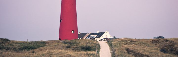 Ein roter Leuchtturm an der Küste mit einem Weg.