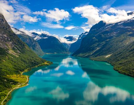 Ein Fjord mit leuchtend blaugrünem Wasser, umgeben von hohen Bergen unter einem bewölkten Himmel.