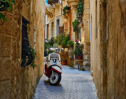 Vespa-Roller steht in einer Gasse mit vielen Pflanzen in Italien 
