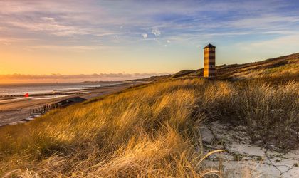 Ein Sandstrand mit Dünen und einem Leuchtturm bei Sonnenuntergang.