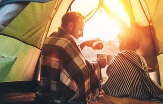 Ein Vater und sein Sohn sitzen gemütlich in einem Zelt, warmes Sonnenlicht fällt herein.