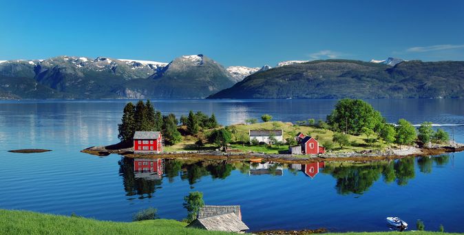 Hardangerfjord im südwestlichen Norwegen im Sommer. Ein rot, norwegische Haus auf einer kleinen Insel im Fjord. In der Ferne den Folgefonna Gletscher. 