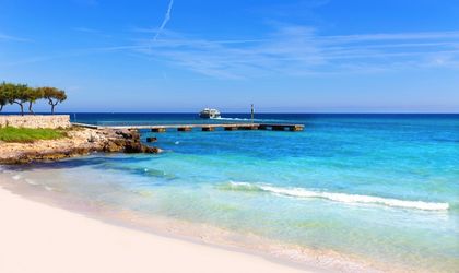 Ein Sandstrand mit türkisblauem Wasser und einem bewölkten Himmel.