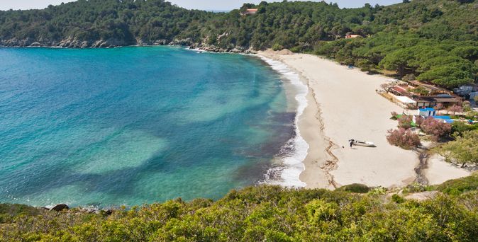 Ein Sandstrand mit türkisfarbenem Wasser, umgeben von Hügeln.