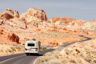 Camper fährt auf einer langen Straße umgeben von roten Felsen in den USA