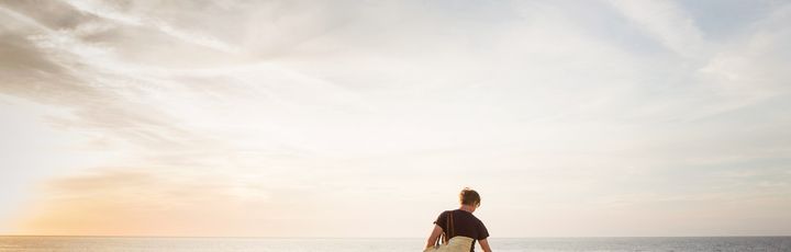 Eine einzelne Person geht am Strand entlang, während die untergehende Sonne den Himmel in warme Orangetöne taucht und sich im ruhigen Meer spiegelt.