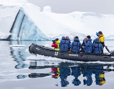 Kanufahrer fahren auf dem Meer im Hintgergrund ein Eisberg