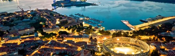 Eine Luftaufnahme von Pula, Kroatien, bei Nacht, mit dem beleuchteten Amphitheater.