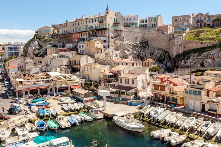 Eine malerische Küstenstadt mit vielen Booten, die im Hafen liegen. Die Häuser sind in warmen Farben gehalten und schmiegen sich an den Hang, während sich das Meer bis zum Horizont erstreckt.