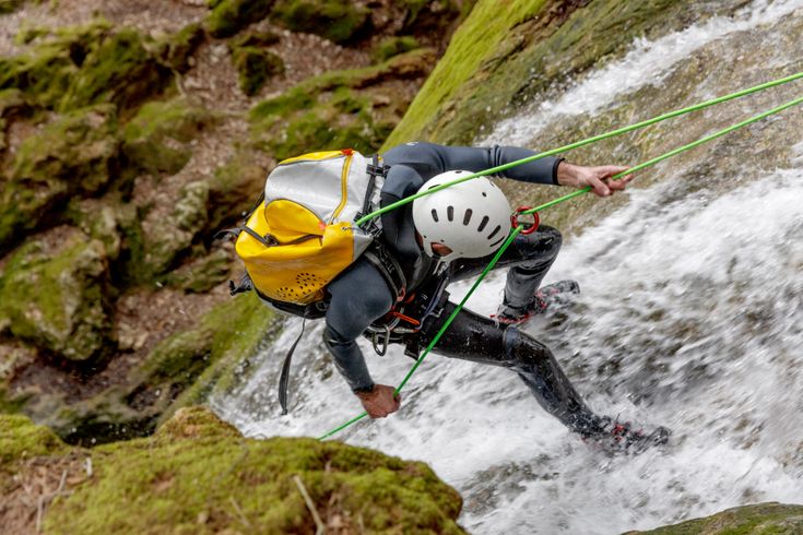 Ein Mann klettert an einer Felswand, während Wasser unter ihm lang fließt.