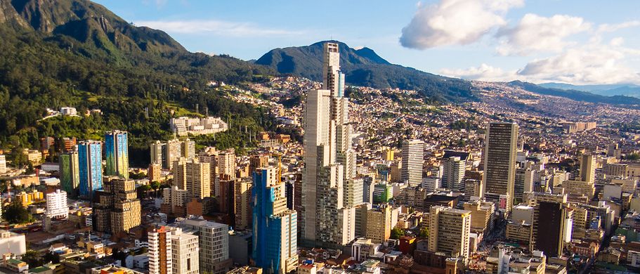 Die Skyline von Bogotá, Kolumbien, bei Sonnenuntergang, mit zahlreichen Hochhäusern und Wolkenkratzern, die sich unter einem orangefarbenen Himmel erheben.