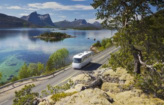 Landschaftsblick auf einen ruhigen Fjord, umgeben von grünen Hügeln und Bergen unter blauem Himmel.