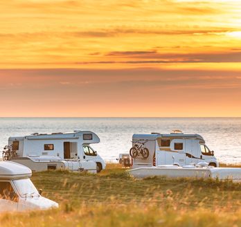 Weißer Campervan steht an einem Fjordufer in Norwegen bei Sonnenuntergang, umgeben von Bergen.