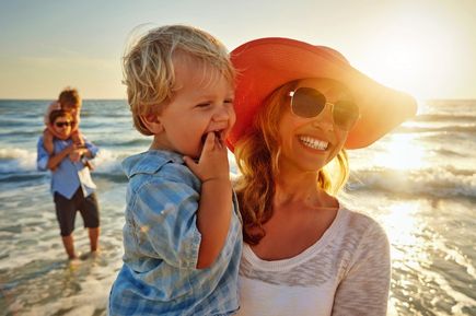 Eine Frau hält ein Kind im Arm am Strand.