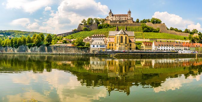 Eine atemberaubende Aussicht auf die Festung Marienberg, die hoch über Würzburg und dem Fluss Main thront, umgeben von grünen Weinbergen und der Stadtkulisse.