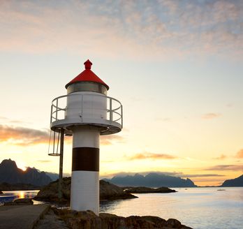 Ein rot-weißer Leuchtturm steht auf einer felsigen Küste bei Sonnenuntergang.