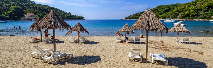 Ein Sandstrand mit Sonnenschirmen und Liegestühlen.