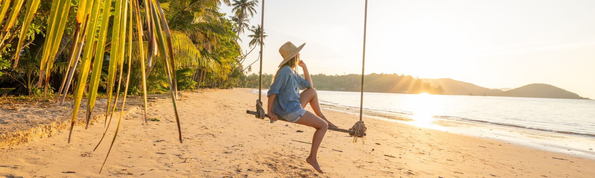 Frau sitzt auf Schaukel an einem Strand mit Meer im Hintergrund
