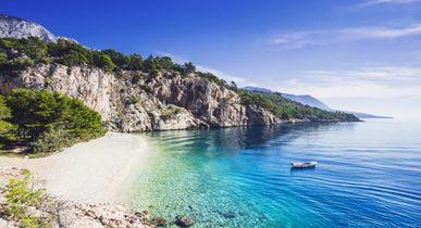 Eine Bucht mit einem Sandstrand und türkisfarbenem Wasser, umgeben von Bergen.