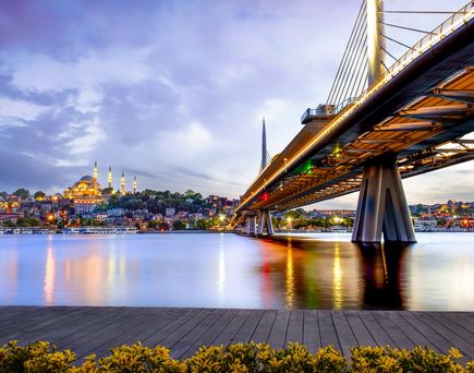 Blick auf Gewässer mit Brücke und beleuchtete Stadt Istanbul in der Türkei bei Abenddämmerung.