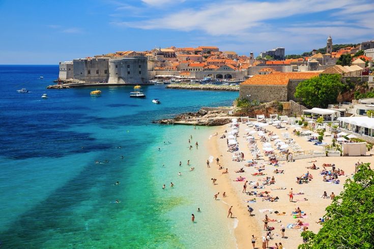 Ein belebter Sandstrand mit vielen Menschen und türkisfarbenem Wasser.
