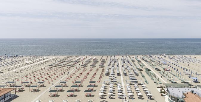 Weitläufiger Sandstrand mit systematisch angeordneten Sonnenliegen und Sonnenschirmen bis zum Meer.