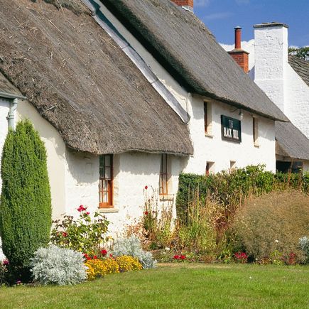 Ein weißes Cottage mit einem Reetdach.