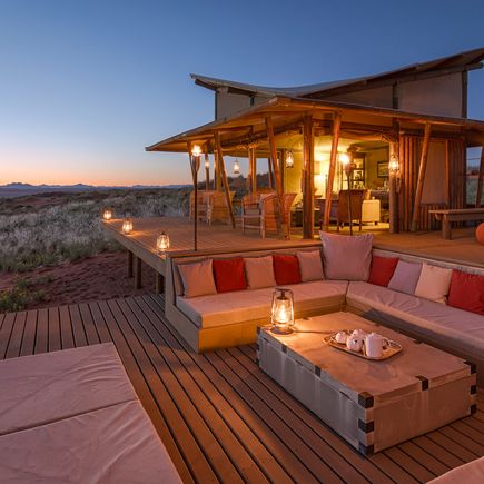 Modernes, beleuchtetes Glamping-Zelt bei Sonnenuntergang, umgeben von Bäumen.