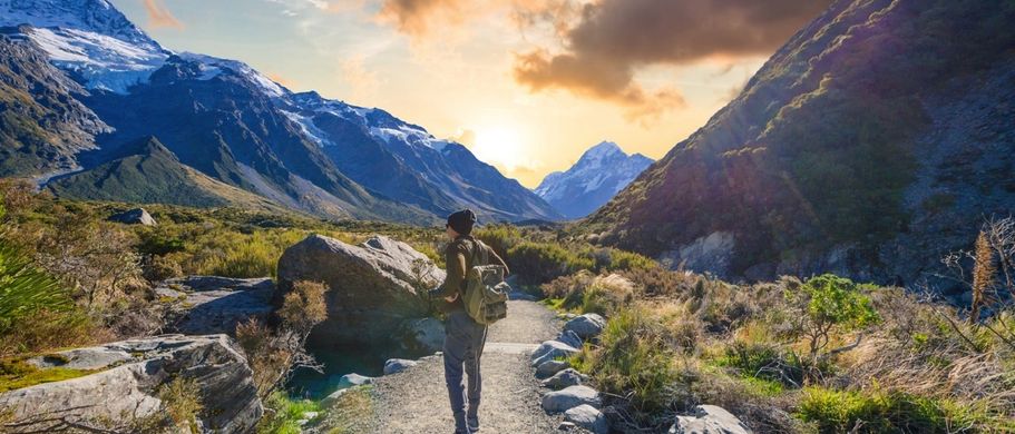 Der majestätische Mount Cook in Neuseeland, der sich mit schneebedeckten Gipfeln über einem malerischen Tal und einem See erhebt, unter einem bewölkten Himmel.