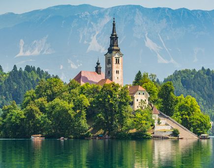 Eine Kirche auf einer Insel im Bleder See in Slowenien, umgeben von Bergen.